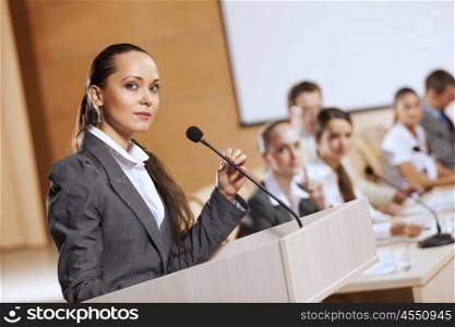 Businesswoman standing on stage and reporting for audience. Speaker at stage