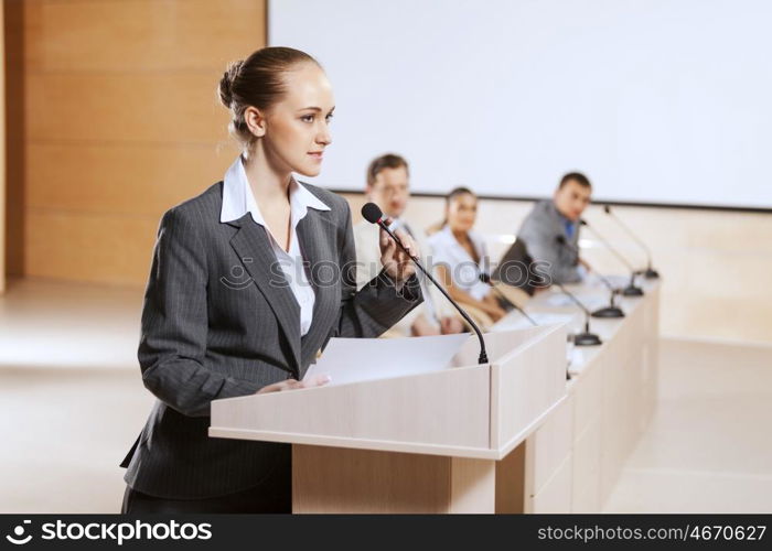 Businesswoman standing on stage and reporting for audience. Speaker at stage