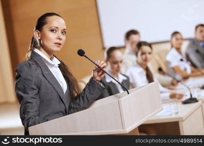 Businesswoman standing on stage and reporting for audience. Speaker at stage