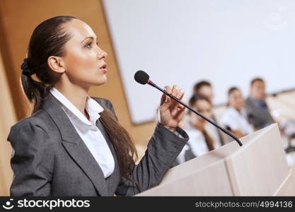 Businesswoman standing on stage and reporting for audience. Speaker at stage