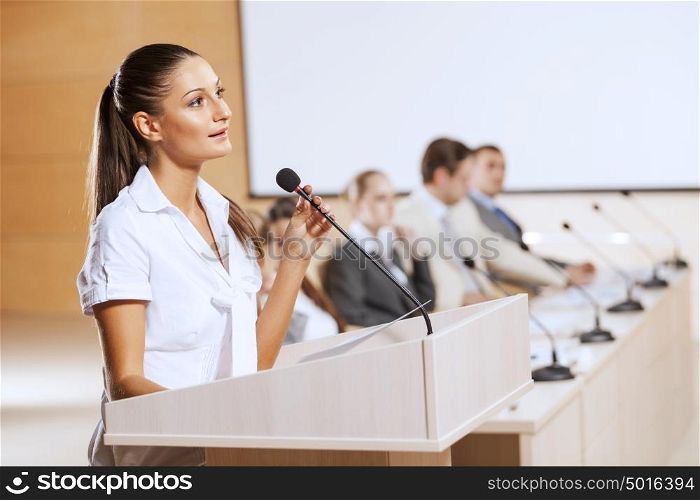 Businesswoman standing on stage and reporting for audience. Speaker at stage