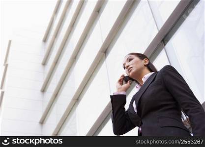 Businesswoman standing outdoors by building on cellular phone (high key/selective focus)