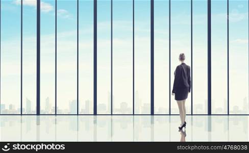 Businesswoman standing with back and looking in office window. Office life