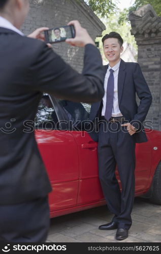Businesswoman Taking Businessman&rsquo;s Picture Next to His Car