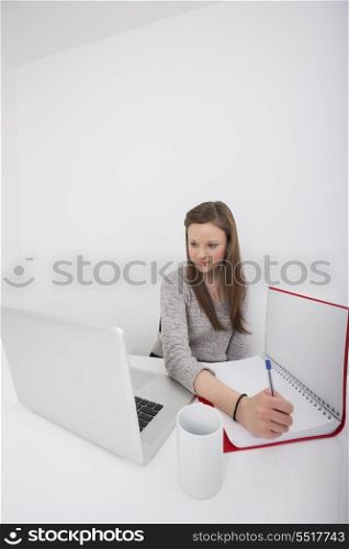 Businesswoman taking notes while looking at laptop in office
