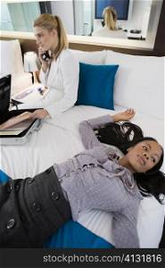 Businesswoman talking on a cordless phone and another businesswoman lying on the bed
