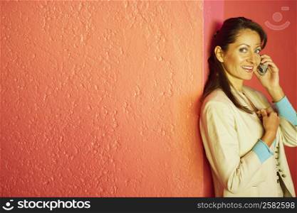 Businesswoman talking on a mobile phone and leaning against a wall
