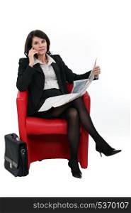 Businesswoman talking on her mobile phone while reading the newspaper