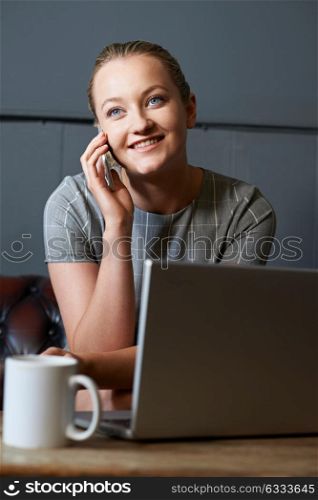 Businesswoman Talking On Mobile Phone Working On Laptop In Internet Cafe