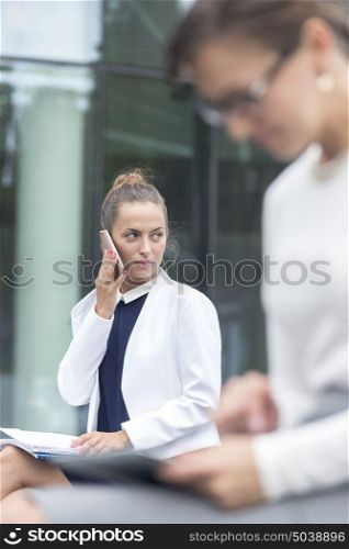 Businesswoman talking on smartphone while sitting against office