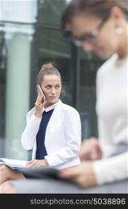 Businesswoman talking on smartphone while sitting against office