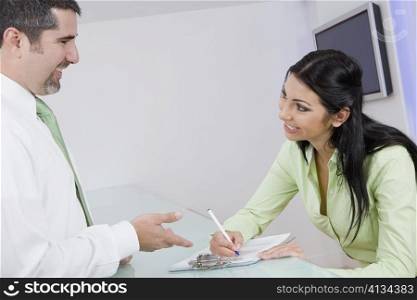Businesswoman talking to a businessman while writing