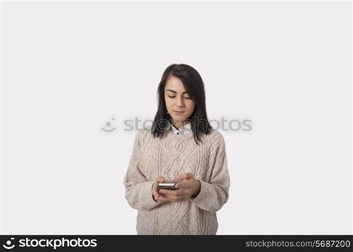 Businesswoman text messaging through smart phone against gray background