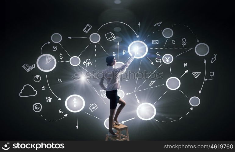 Businesswoman touching connection icon. Back view of businesswoman standing on chair and reaching infographs on wall