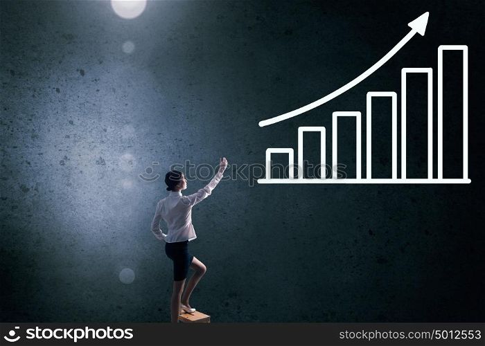 Businesswoman touching graph. Back view of businesswoman standing on chair and reaching infographs on wall