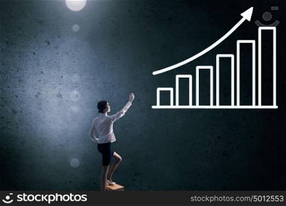Businesswoman touching graph. Back view of businesswoman standing on chair and reaching infographs on wall