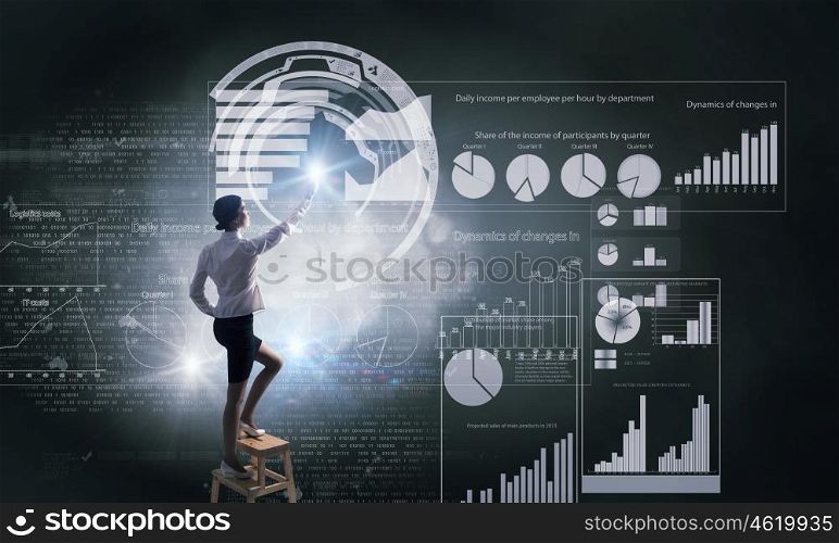 Businesswoman touching icon. Back view of businesswoman standing on chair and reaching infographs on wall