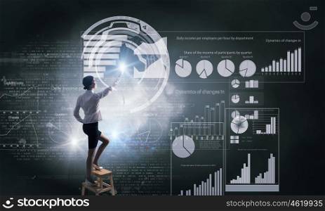 Businesswoman touching icon. Back view of businesswoman standing on chair and reaching infographs on wall