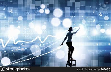 Businesswoman touching icon on screen. Back view of businesswoman standing on chair and reaching infographs on wall