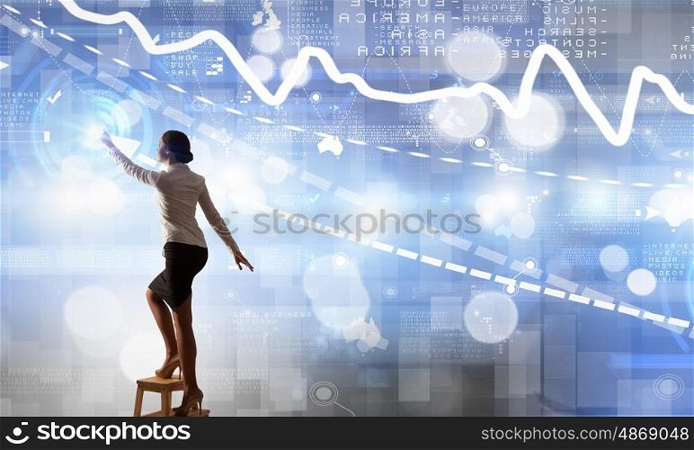 Businesswoman touching icon on screen. Back view of businesswoman standing on chair and reaching infographs on wall
