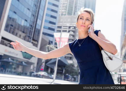 Businesswoman trying to catch a taxi in business cuty district. Waving for a taxi in city