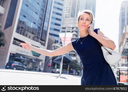 Businesswoman trying to catch a taxi in business cuty district. Waving for a taxi in city