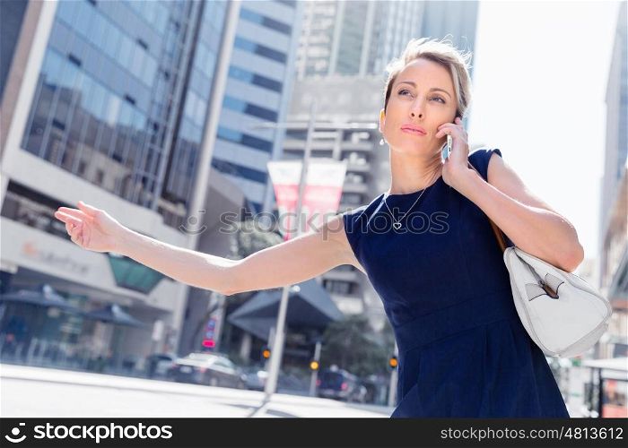 Businesswoman trying to catch a taxi in business cuty district. Waving for a taxi in city