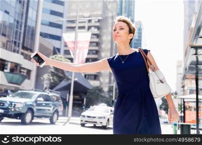 Businesswoman trying to catch a taxi in business cuty district. Waving for a taxi in city
