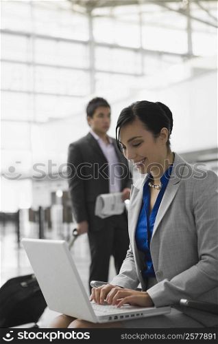 Businesswoman using a laptop and a businessman pulling his luggage behind her