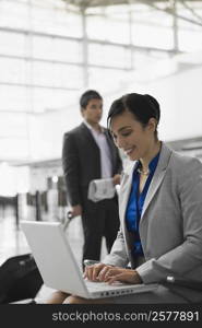 Businesswoman using a laptop and a businessman pulling his luggage behind her