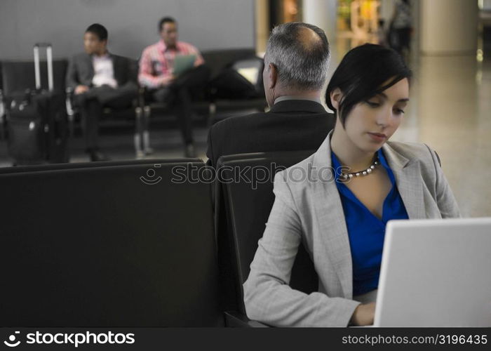 Businesswoman using a laptop with a businessman behind him at an airport