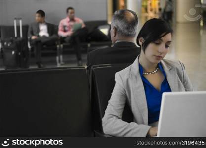 Businesswoman using a laptop with a businessman behind him at an airport