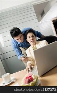 Businesswoman using a laptop with a businessman holding a mobile phone standing behind her