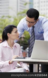Businesswoman using a laptop with a businessman standing beside her
