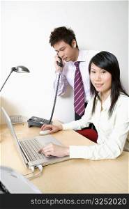 Businesswoman using a laptop with a businessman talking on the telephone
