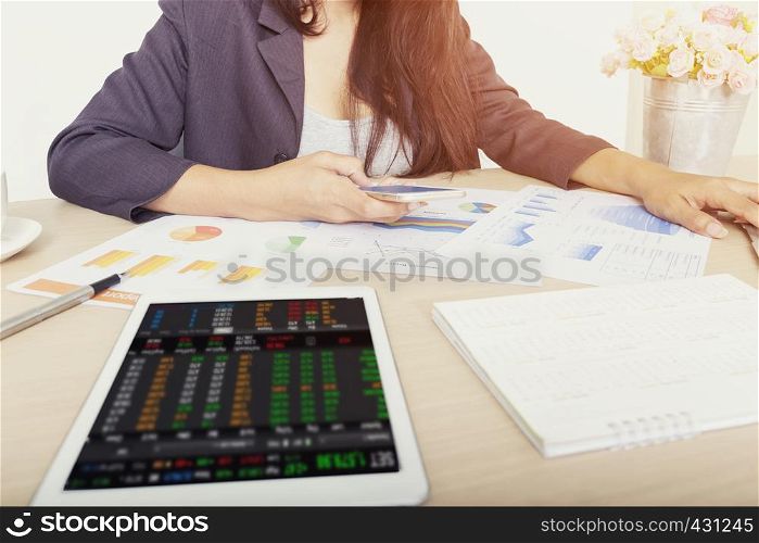 Businesswoman using analyzing investment charts with digital data on mobile and tablet on wooden desk at office.