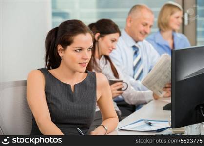 Businesswoman using computer with colleagues in background at office