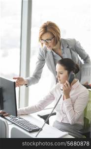 Businesswoman using landline phone while manager pointing towards computer in office
