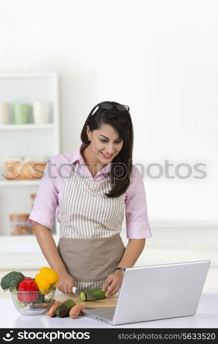 Businesswoman using laptop while chopping vegetable in kitchen