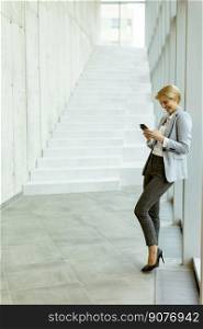 Businesswoman using mobile phone while standing on the modern office hallway