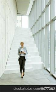 Businesswoman using mobile phone while walking on the modern office hallway