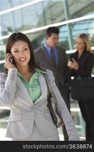 Businesswoman using mobile phone with colleagues in background, outdoors