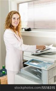 Businesswoman using photocopier in office. Smiling business woman operating photocopy machine in office