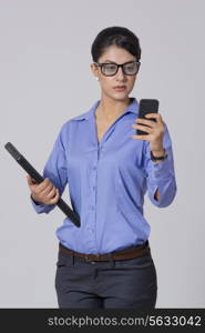 Businesswoman using smart phone while holding laptop against gray background
