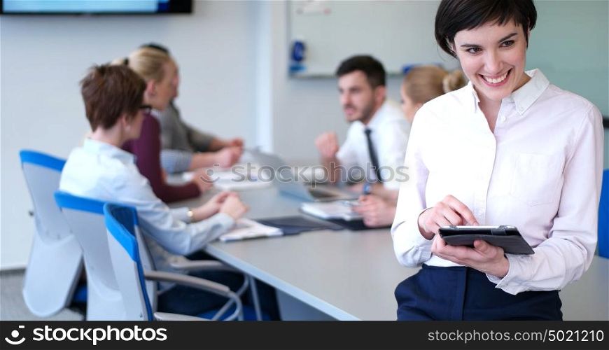 Businesswoman using tablet with coworkers in backgorund having meeting