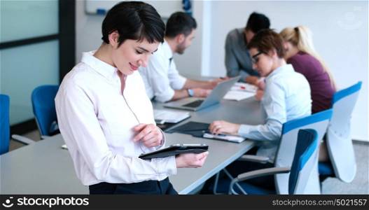 Businesswoman using tablet with coworkers in backgorund having meeting