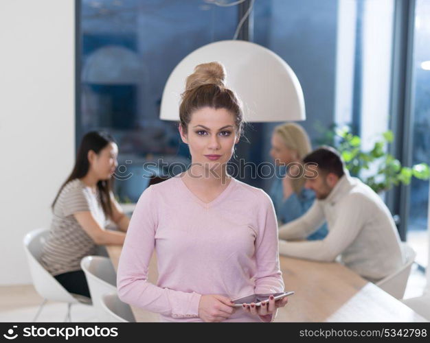 Businesswoman using tablet with coworkers in backgorund having meeting