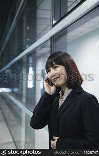 Businesswoman using the phone by a glass wall, Beijing