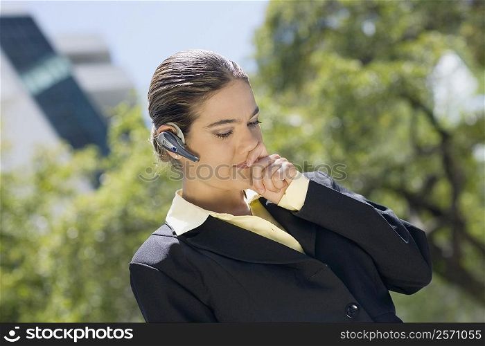 Businesswoman wearing a bluetooth device with her hands covering her mouth