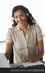 Businesswoman wearing headset in office by laptop smiling (high key/selective focus)